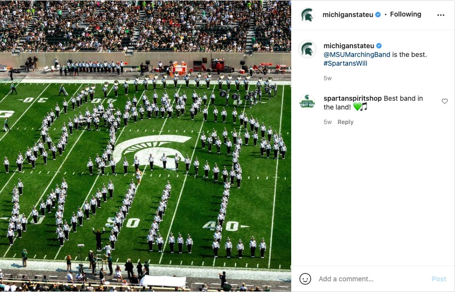 An Instagram screenshot of the Spartan Marching Band forming a helmet with the word WILL spelled out below it. The post by @MichiganStateU has a caption reading "@MSUMarchingBand is the best. #SpartansWill" and a reply from @spartanspiritshop reading "Best band in the land!" with a green heart emoji and a music note emoji.